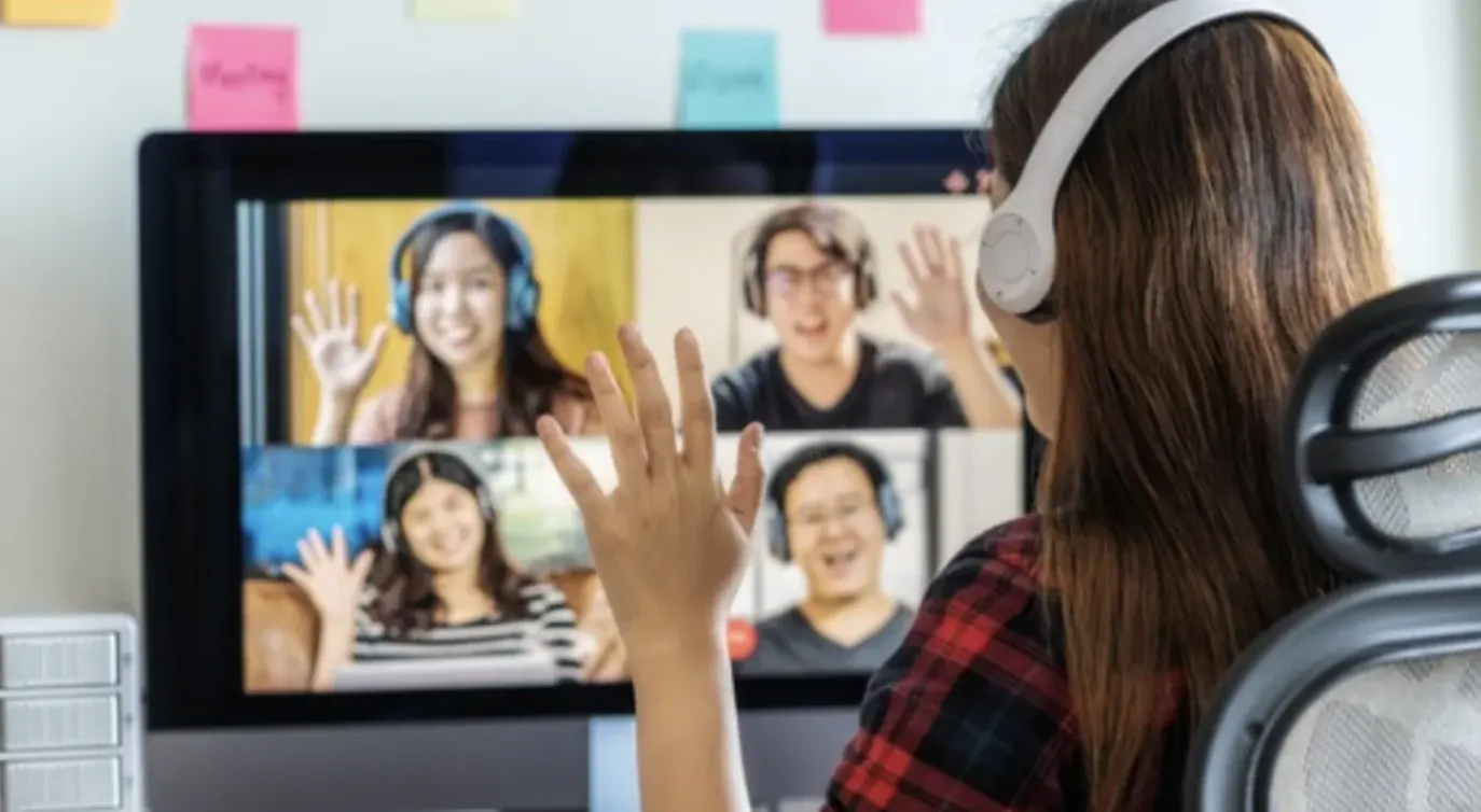 Una mujer con audífonos saluda a sus compañeros en una videollamada.